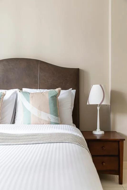 Un dormitorio con una cama bien tendida, cojines estampados y una lámpara de mesita.