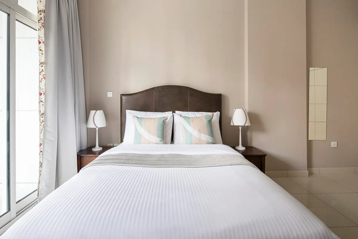Un dormitorio con una cama bien hecha y cortinas junto a una puerta de vidrio.