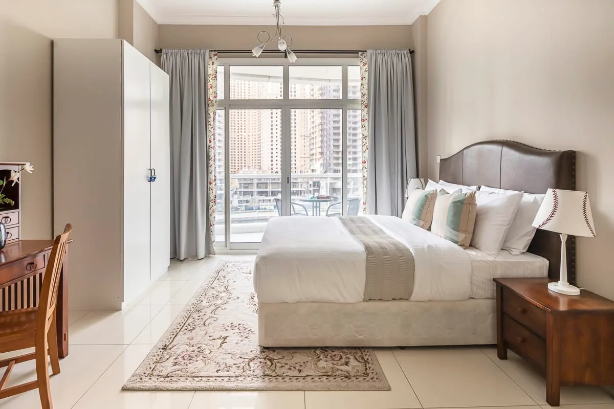 Un dormitorio luminoso con una cama tendida junto a una ventana grande.