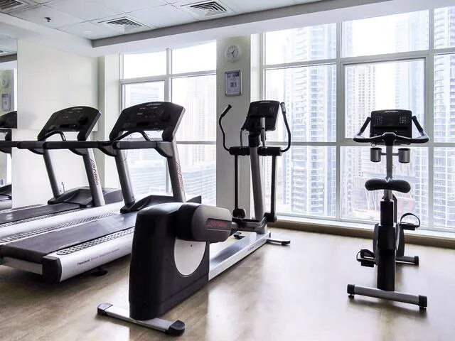 Un gimnasio con máquinas de ejercicio junto a grandes ventanas.