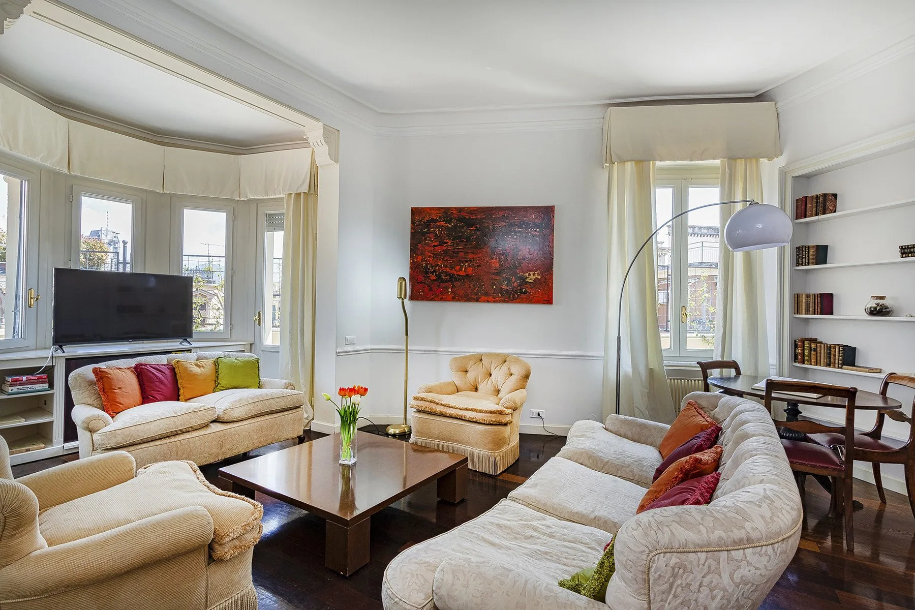 A bright living room with seating, large windows, and a painting on the wall.