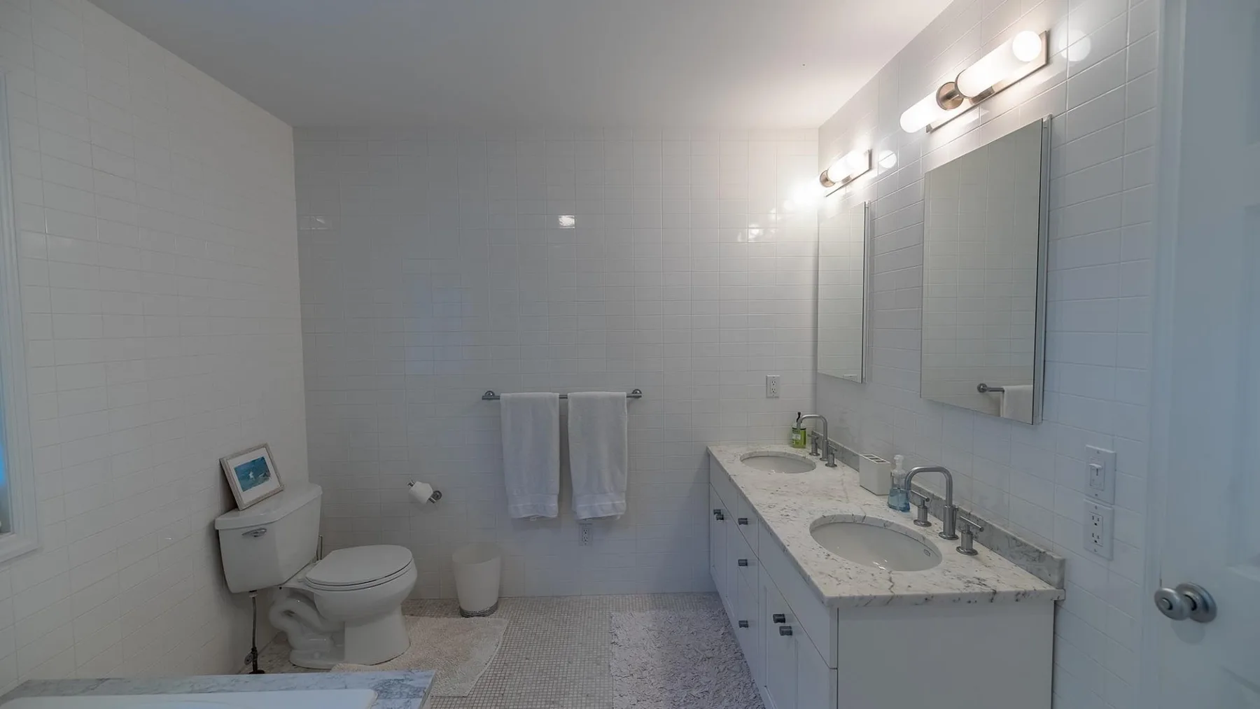 Un baño con azulejos, un inodoro, toallas y un largo tocador con lavabo.