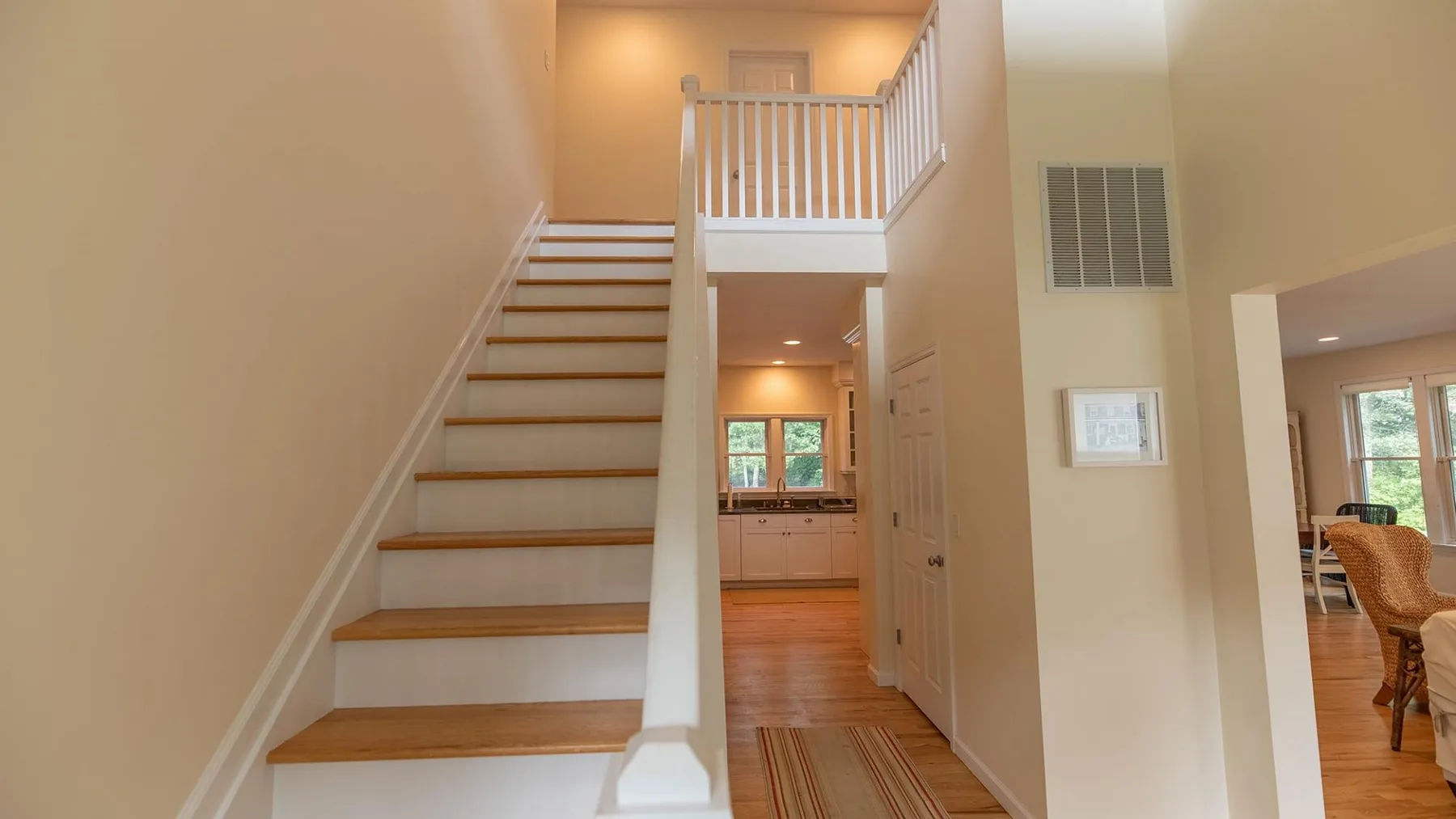 Una escalera y un descanso superior dan a un pasillo luminoso con suelo de madera.