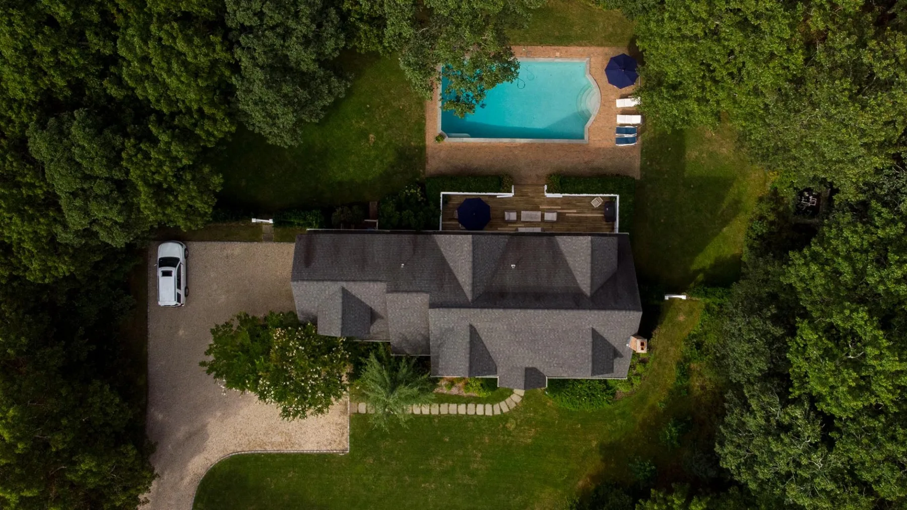 Vista aérea de una casa rodeada de árboles, con una piscina en el jardín.