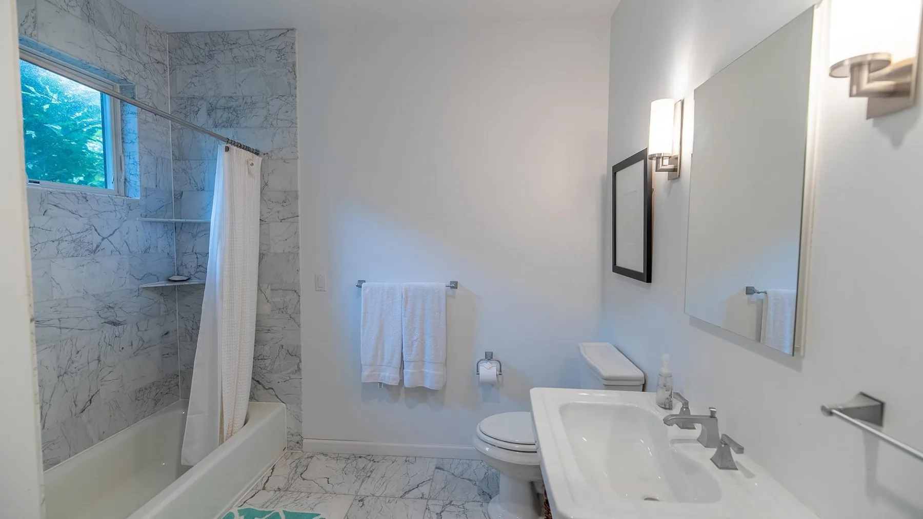 Un baño con ducha revestida de mármol, inodoro y lavabo.