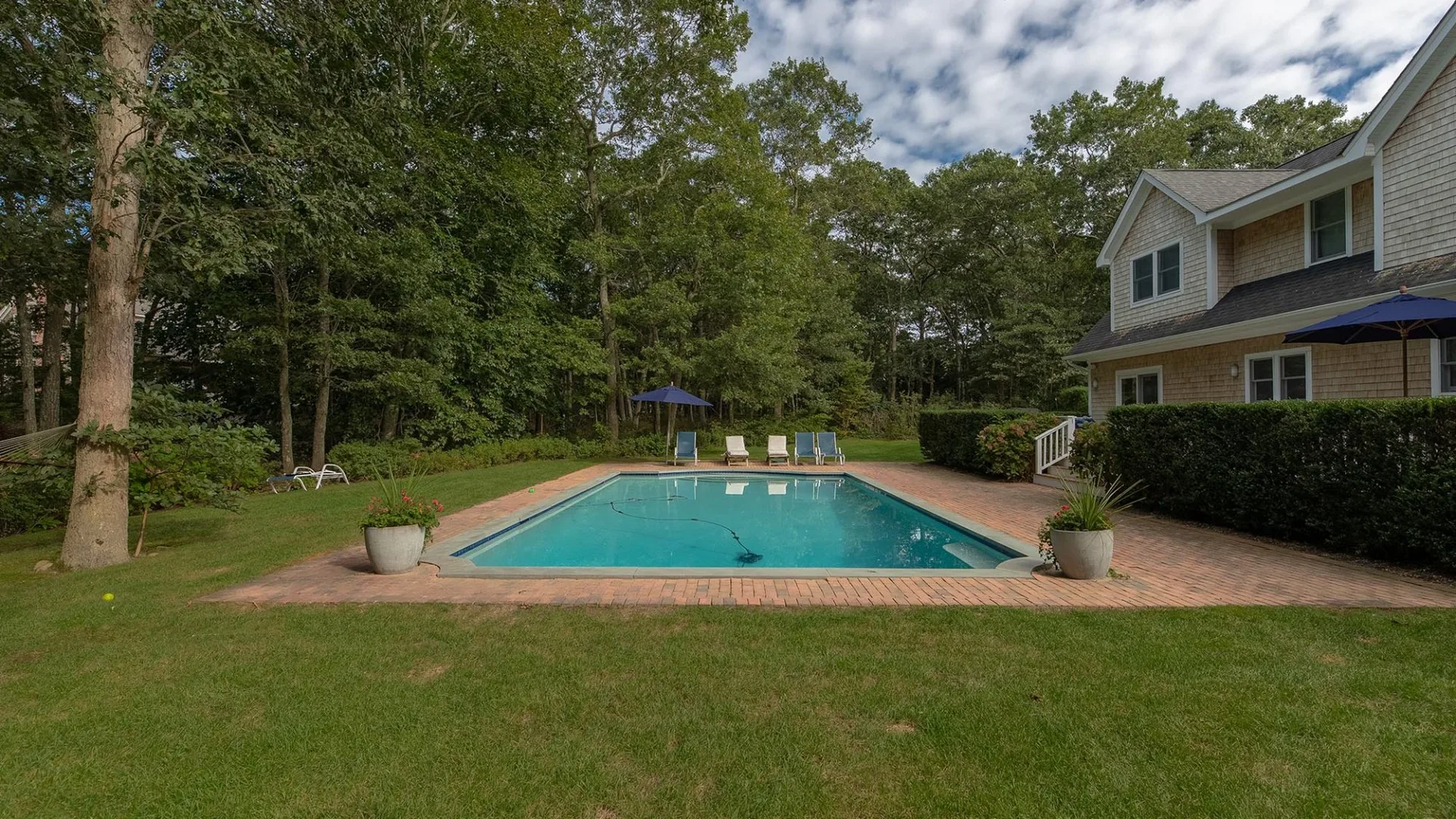 Una piscina al aire libre junto a una casa, rodeada de árboles y césped.