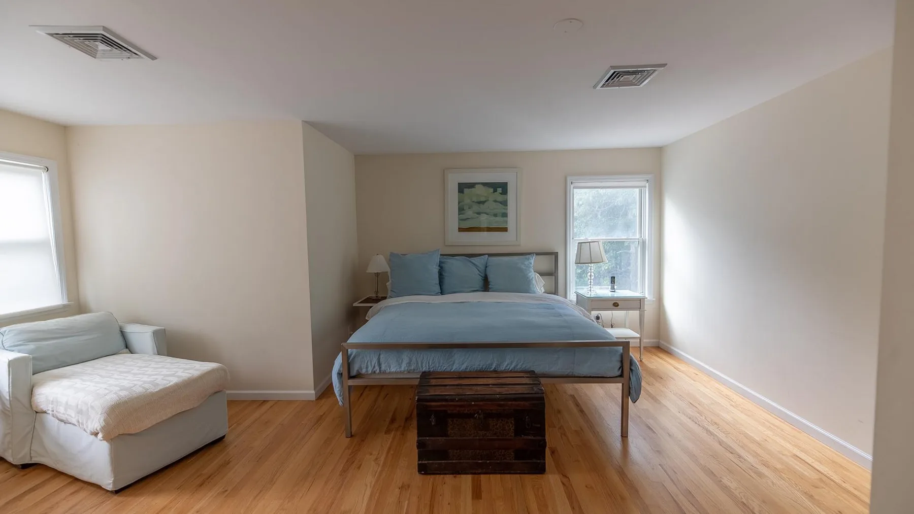 Un dormitorio con una cama, un baúl pequeño al pie y una zona de descanso.