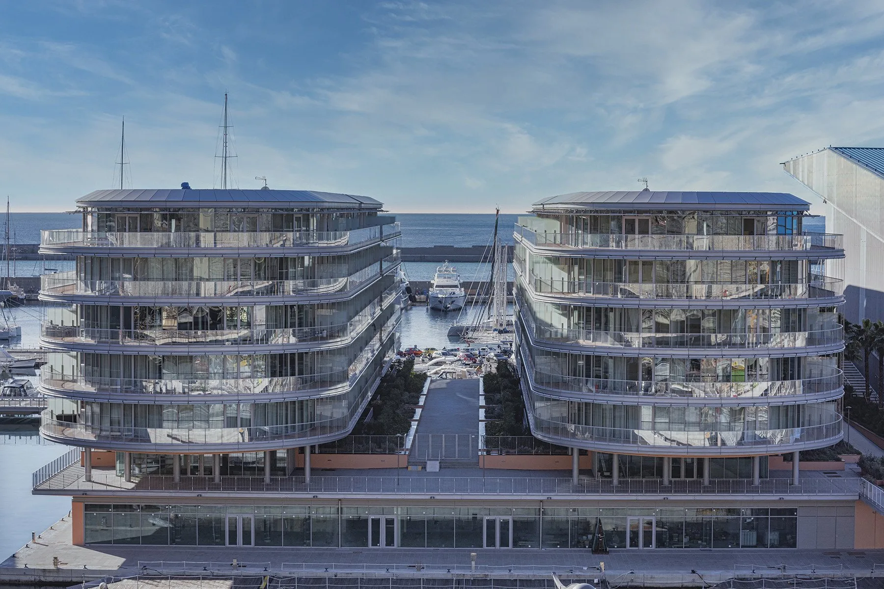 Two modern buildings stand beside the waterfront under a partly cloudy sky.