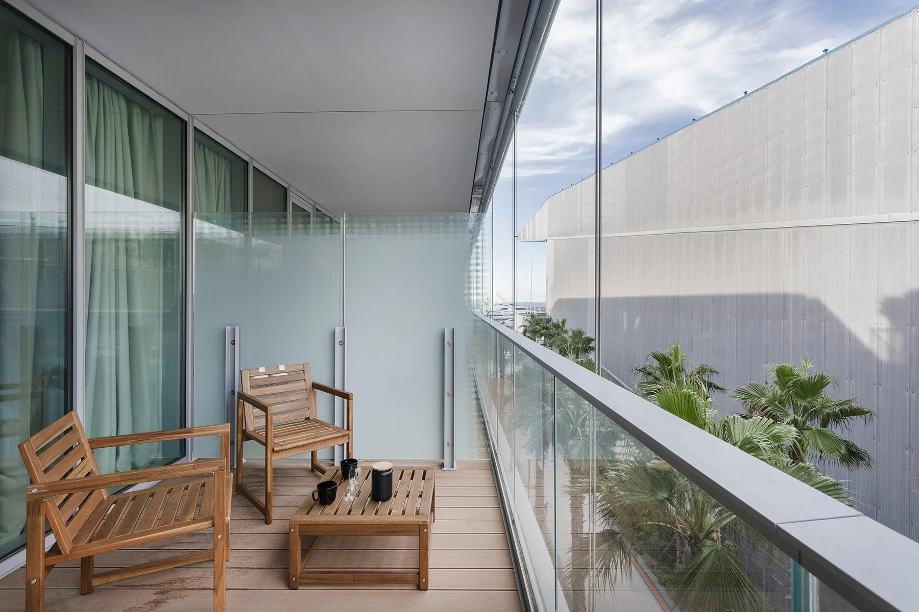 A balcony with wooden seating overlooks nearby buildings and palm trees.