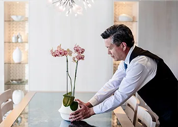 Butler setting an orchid on a dining table.