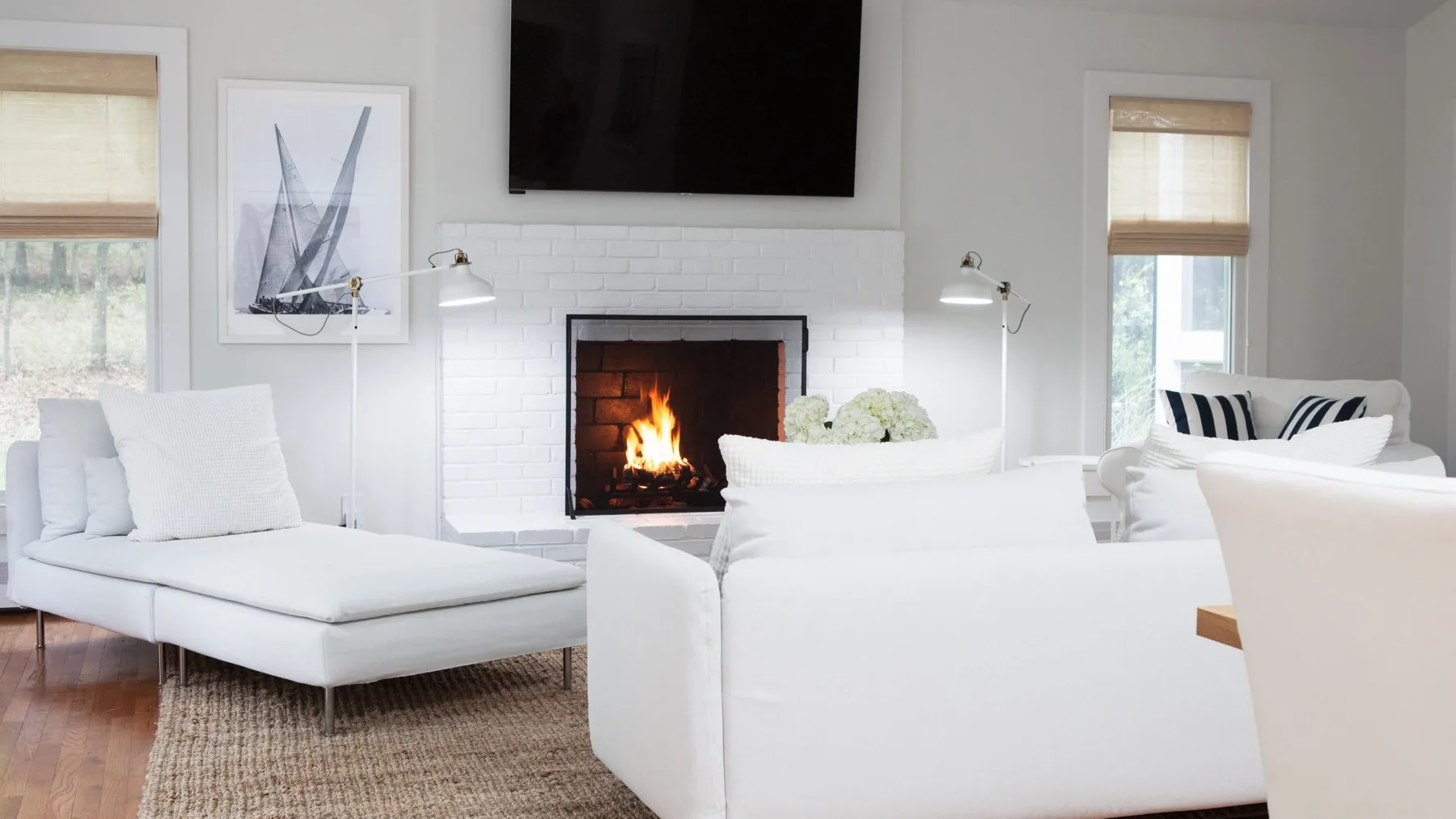 Una sala luminosa con asientos blancos alrededor de una chimenea y un televisor en la pared.