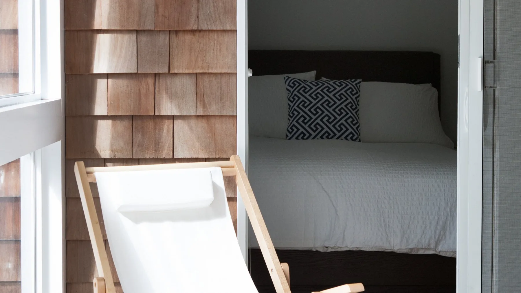 Un dormitorio con una cama y un cojín estampado junto a un biombo de madera.