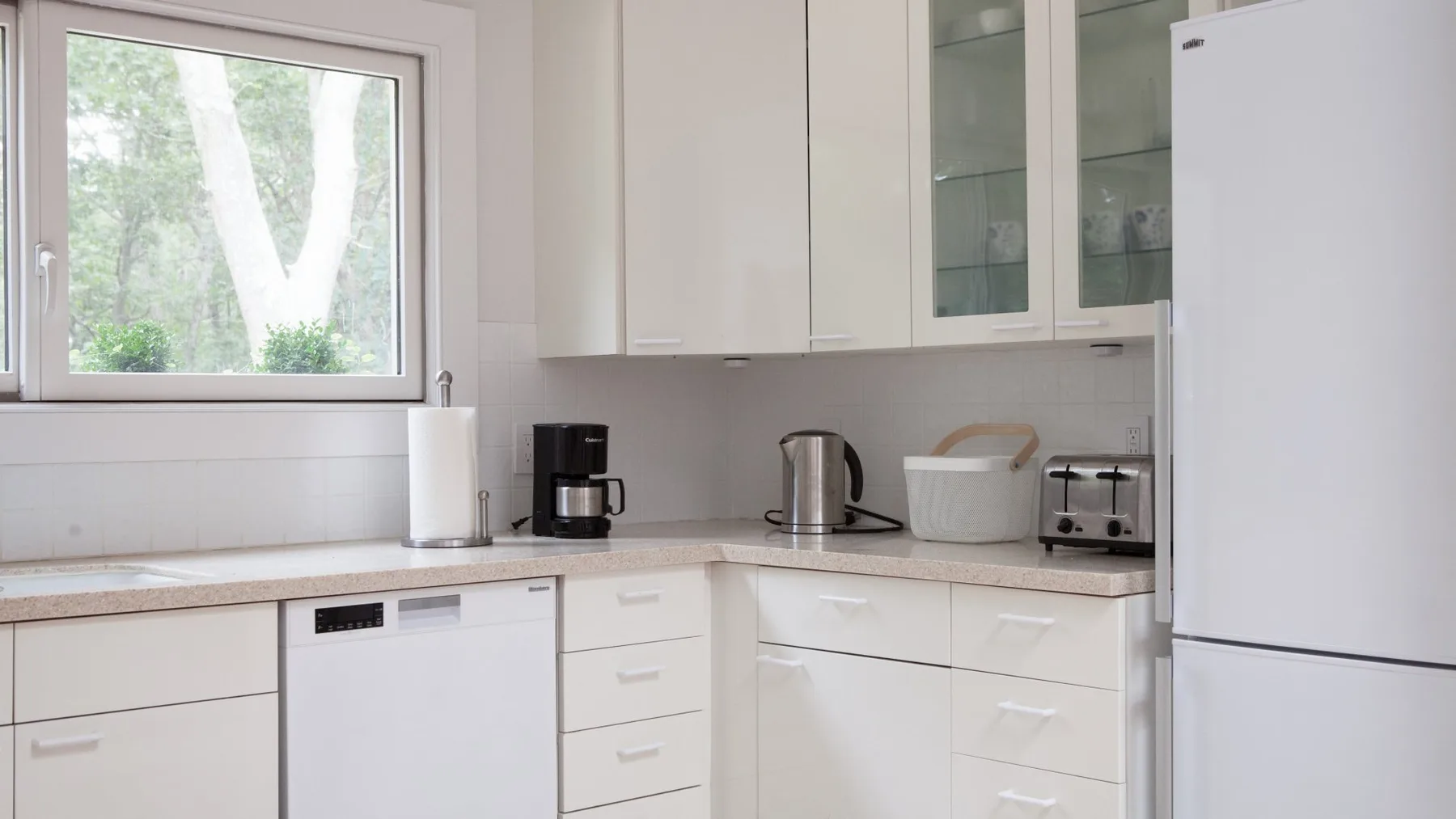 Una cocina luminosa con armarios blancos, una encimera y una ventana con vista a los árboles.