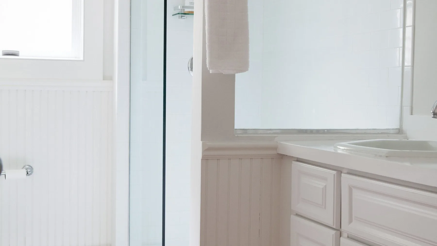 Un baño luminoso con una ducha de vidrio y un mueble de lavabo blanco.