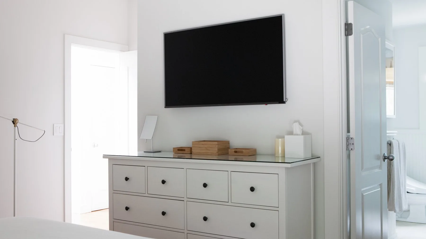 Un dormitorio luminoso con un televisor montado en la pared sobre una cómoda.