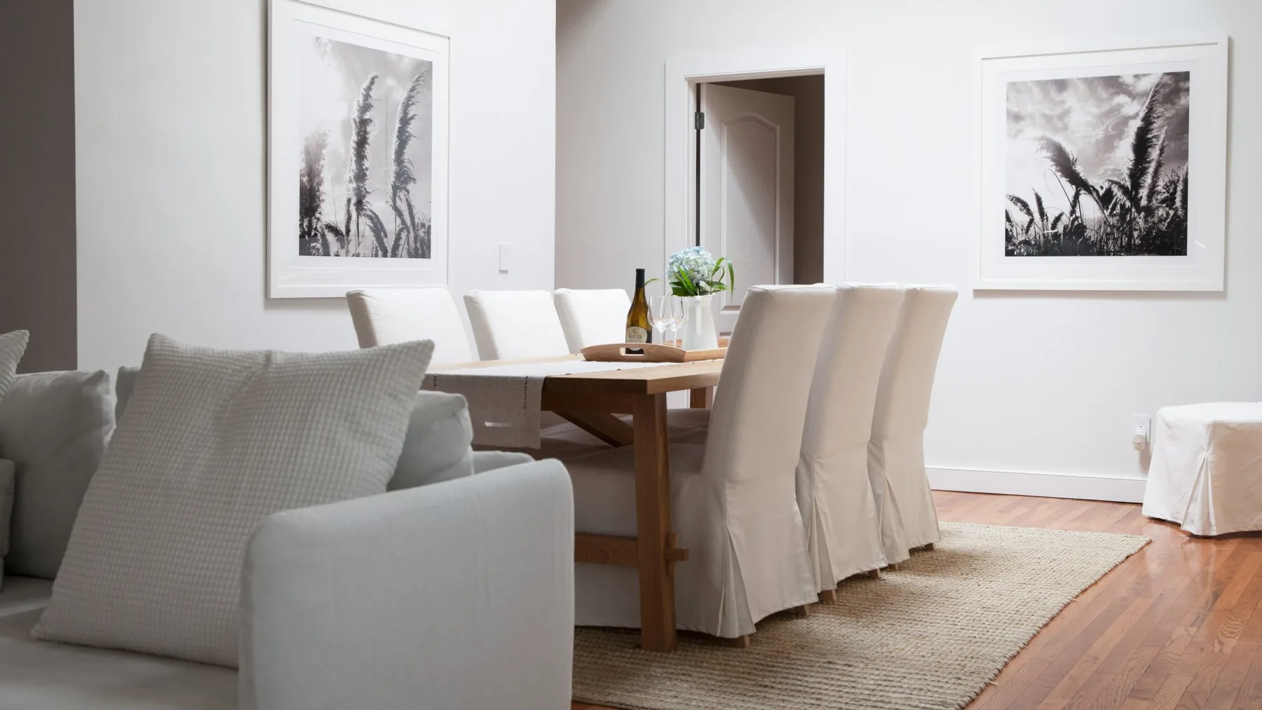 Un comedor luminoso con una mesa de madera, asientos tapizados y láminas botánicas enmarcadas.