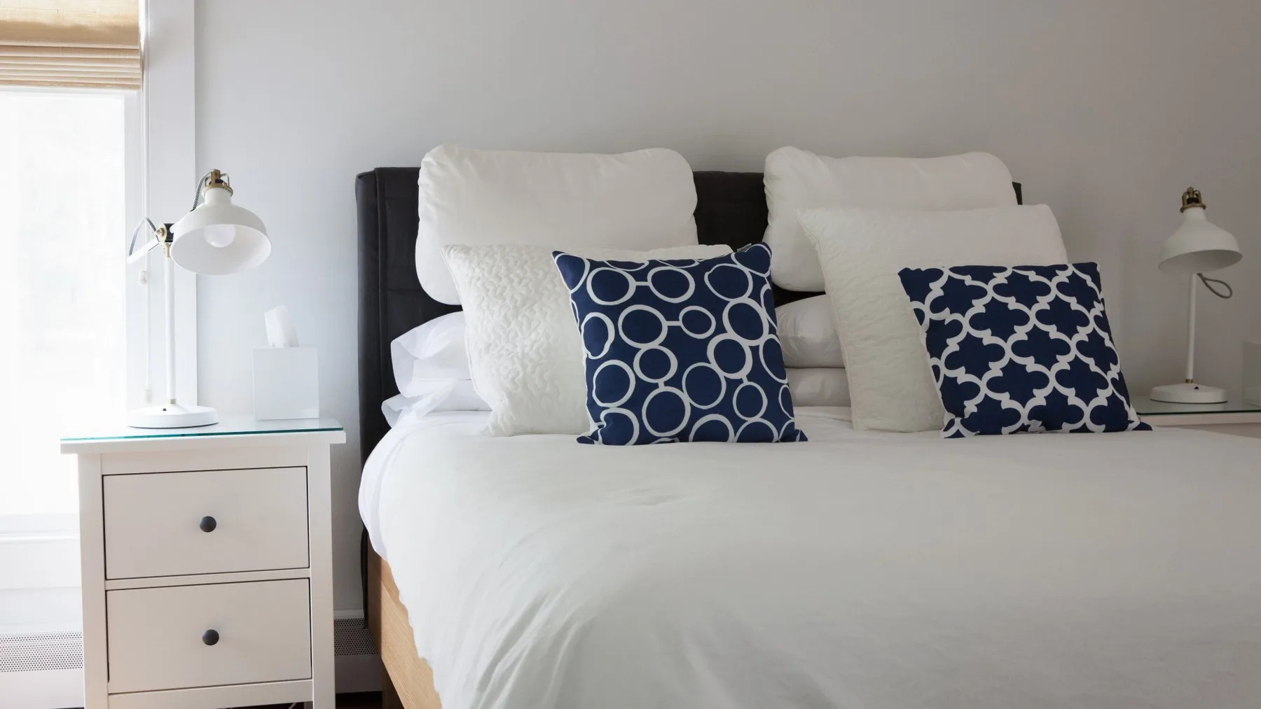 Dormitorio ordenado con ropa de cama blanca y cojines decorativos azules estampados.