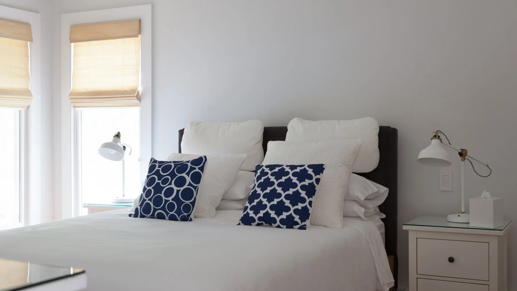 Un dormitorio luminoso con una cama tendida y almohadas estampadas.