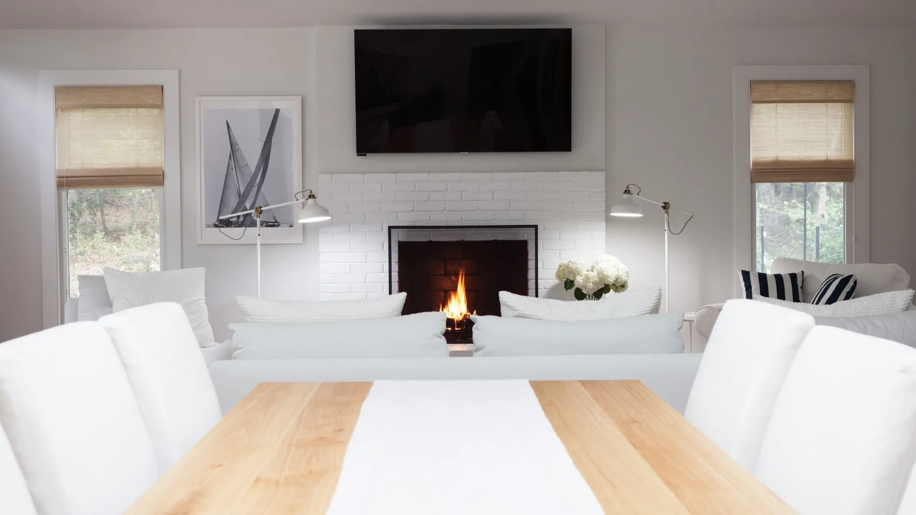 Una sala luminosa con asientos blancos alrededor de una chimenea y un televisor.