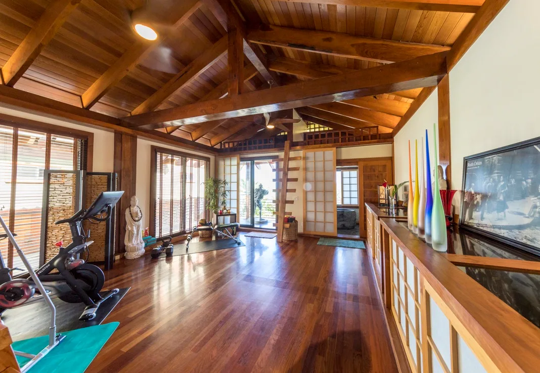 Una amplia sala revestida de madera tiene equipo de ejercicio, colchonetas y grandes ventanas.