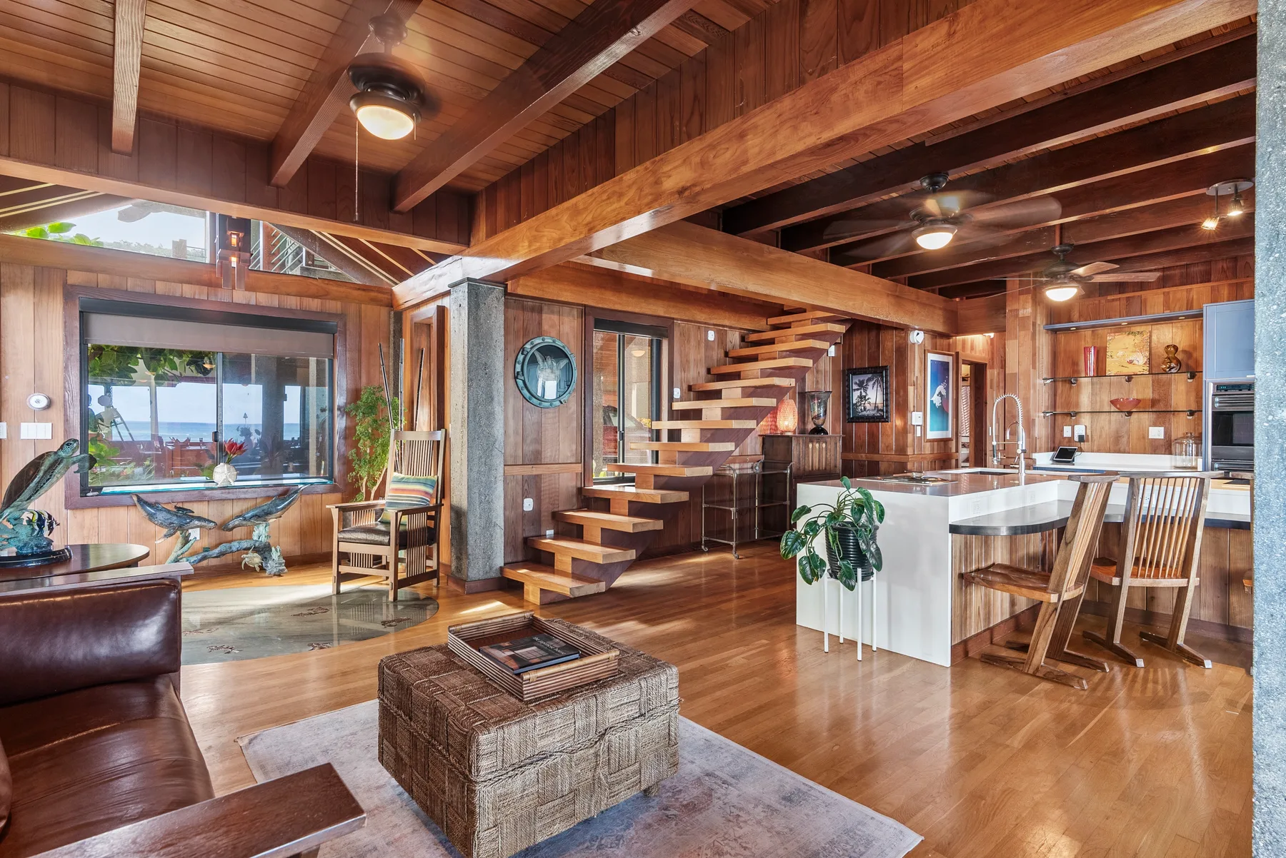 Una sala revestida de madera se abre a una cocina, con una escalera entre ambas.