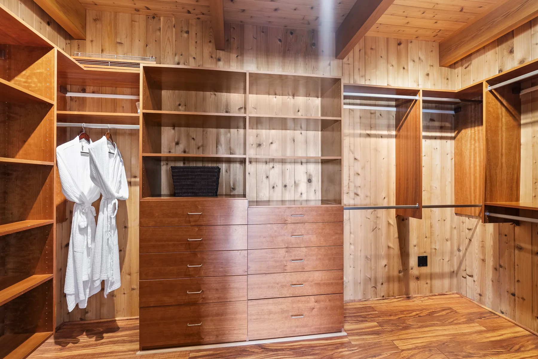 Un vestidor revestido de madera, con estantes abiertos, cajones y ropa colgada.