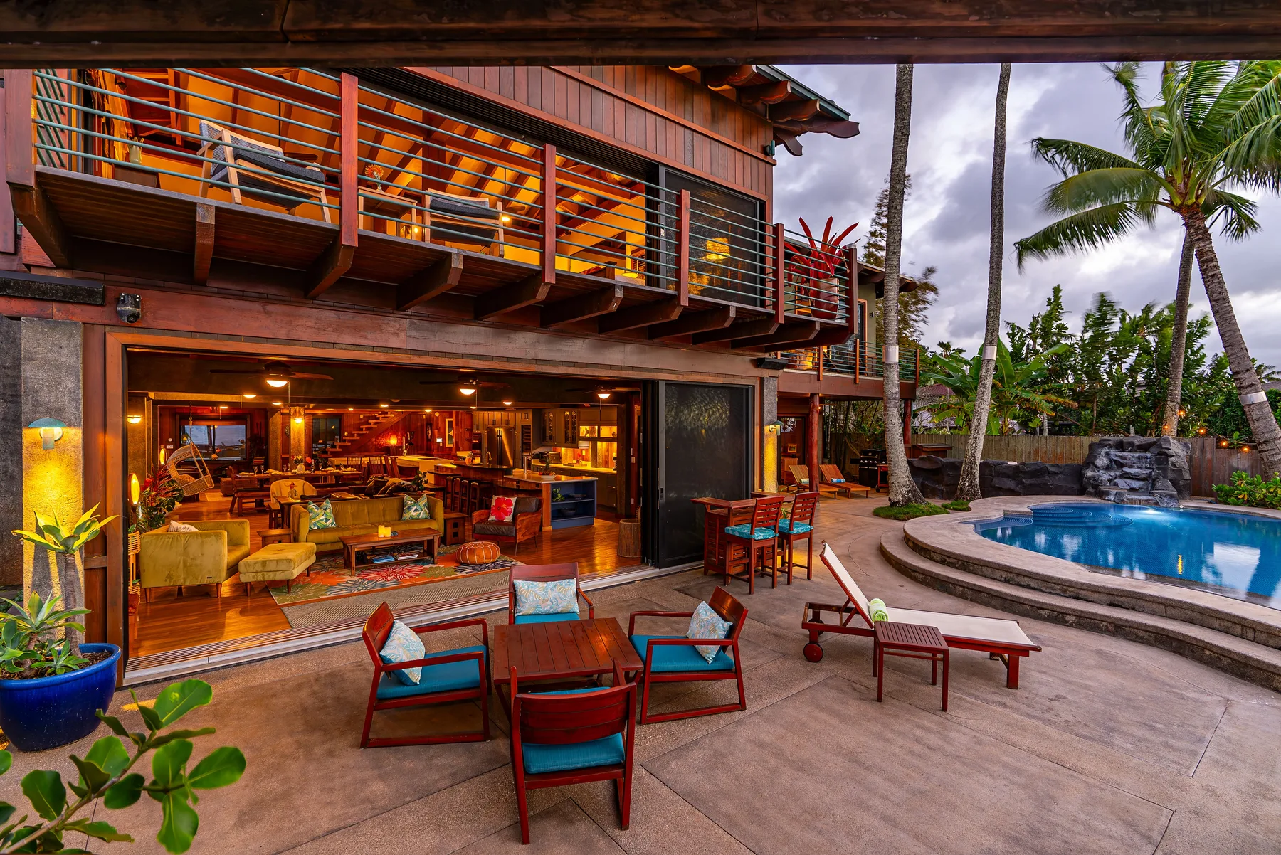 Un patio junto a la piscina con asientos al aire libre y un interior iluminado.