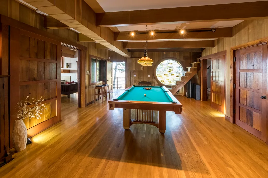 Una sala de juegos revestida de madera tiene una mesa de billar bajo vigas expuestas.