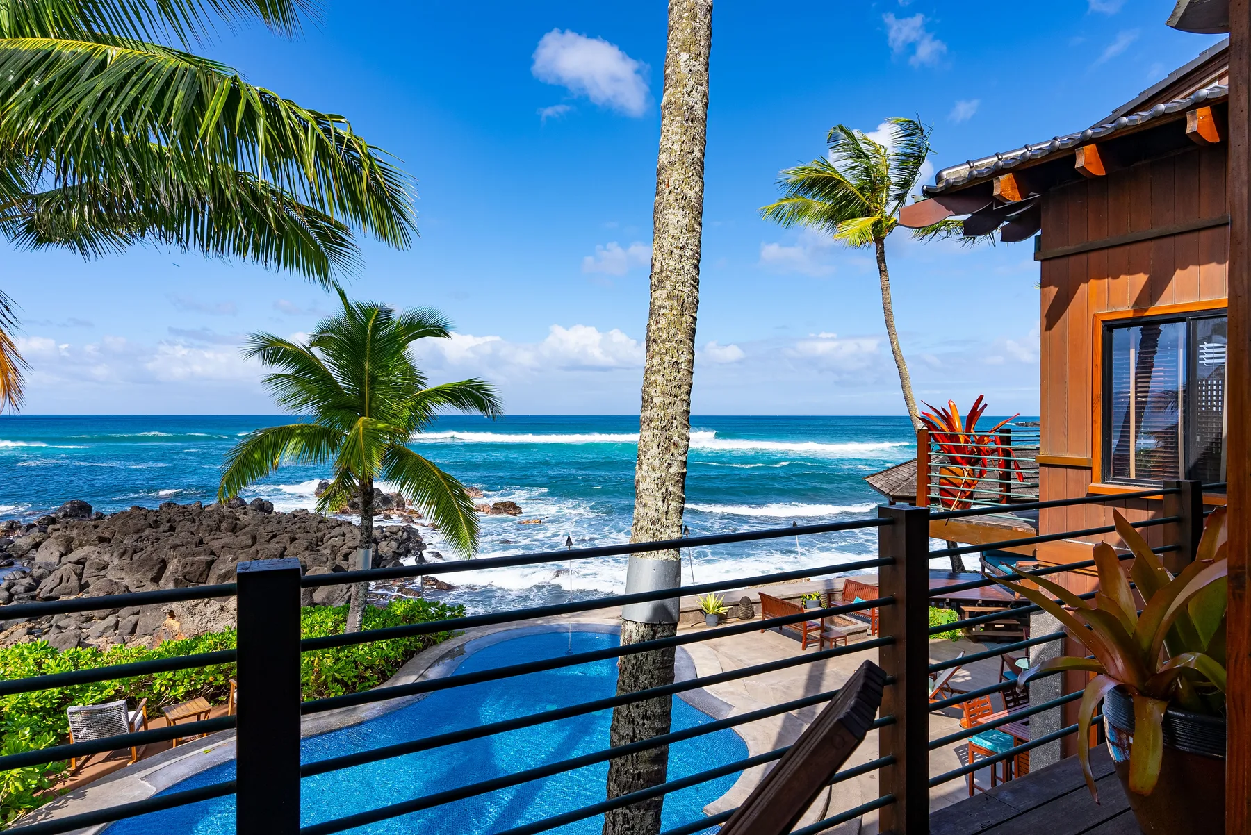Una terraza tropical junto al mar da a una piscina y al océano, con palmeras cerca.