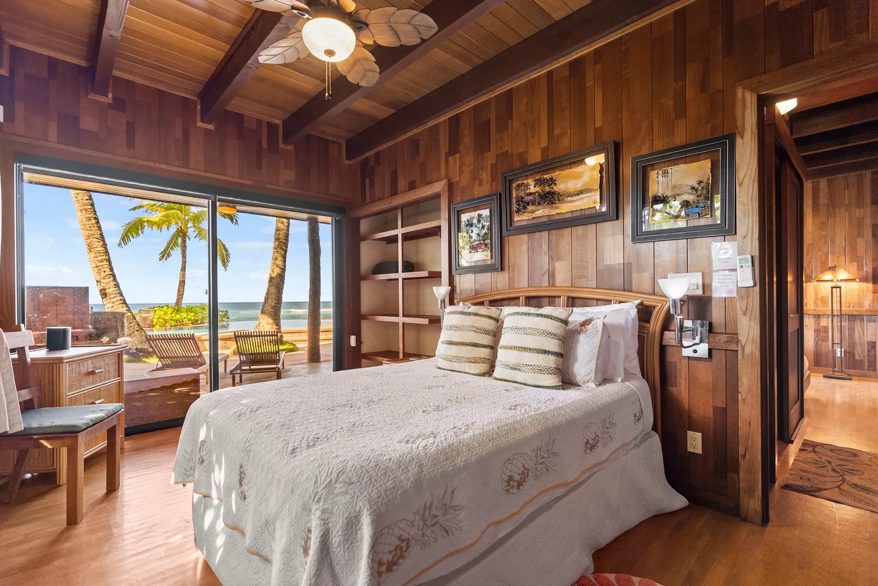 Un dormitorio con una cama junto a grandes puertas corredizas de vidrio que dan a una vista con palmeras.