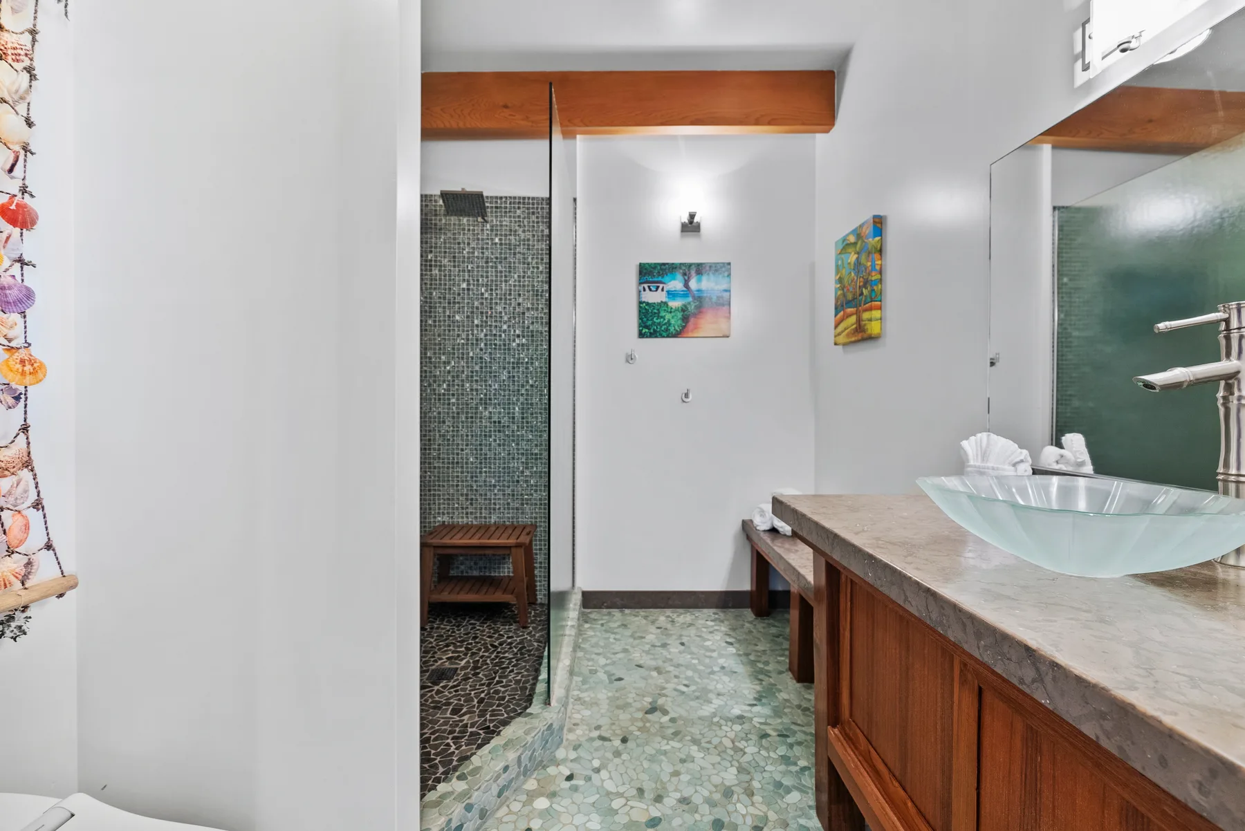 Un baño con un tocador largo, lavabo sobre encimera y zona de ducha con azulejos.