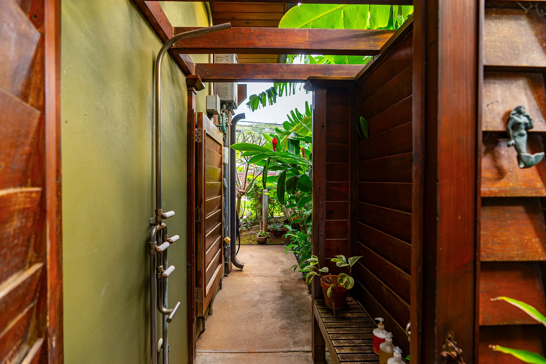 Un pasillo cubierto y estrecho se abre a un jardín frondoso con plantas tropicales.