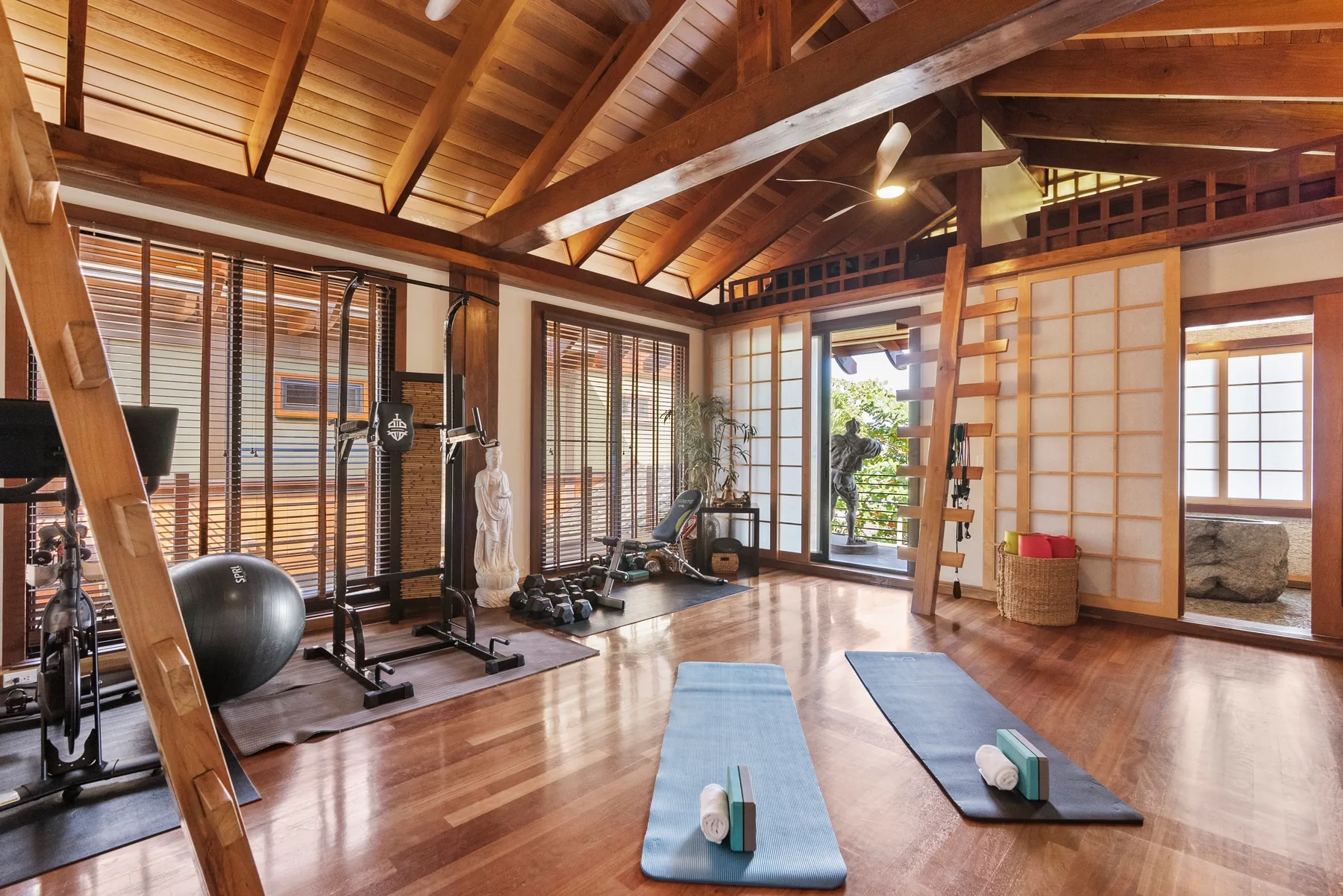 Una sala de ejercicio con vigas de madera, equipo de entrenamiento y colchonetas de yoga.