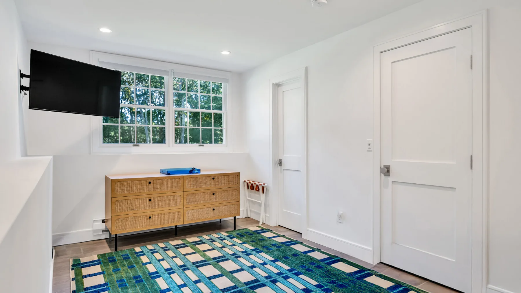 A bright room with a wall-mounted television, a cabinet, and a patterned rug.
