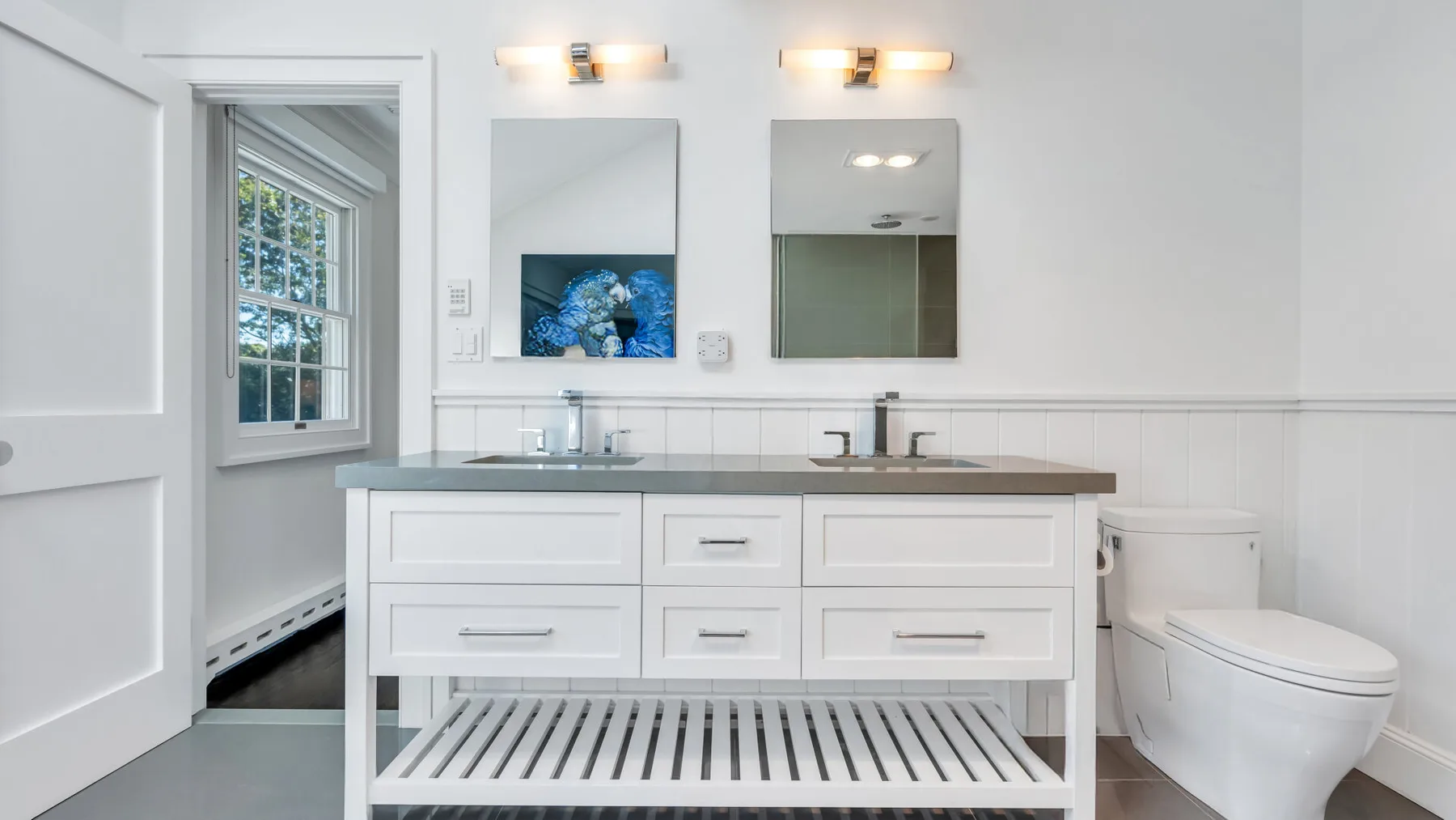 A bright bathroom with a double-sink vanity and a toilet beside it.