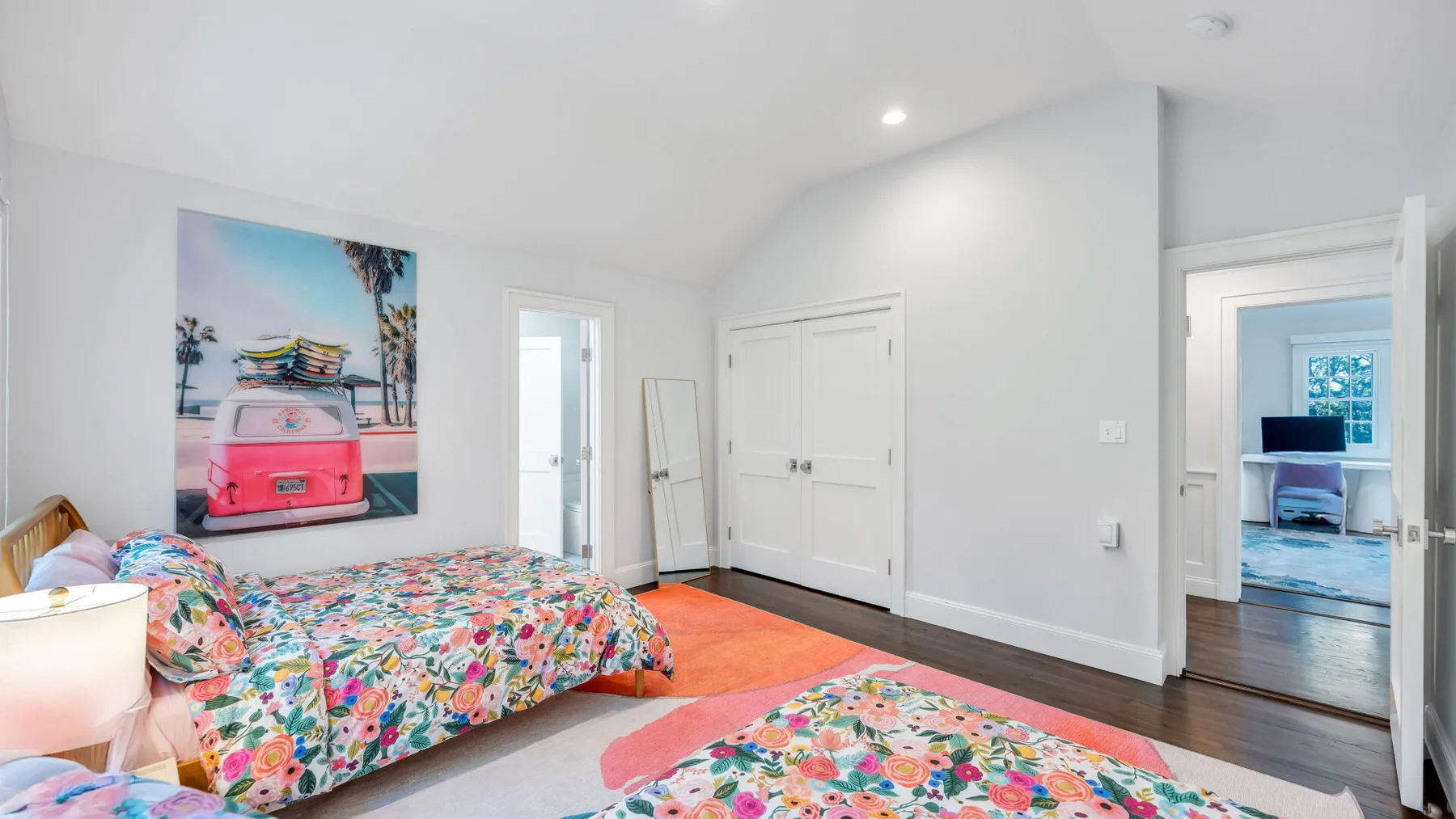 A bright bedroom with colorful floral bedding and a beach-themed wall print.