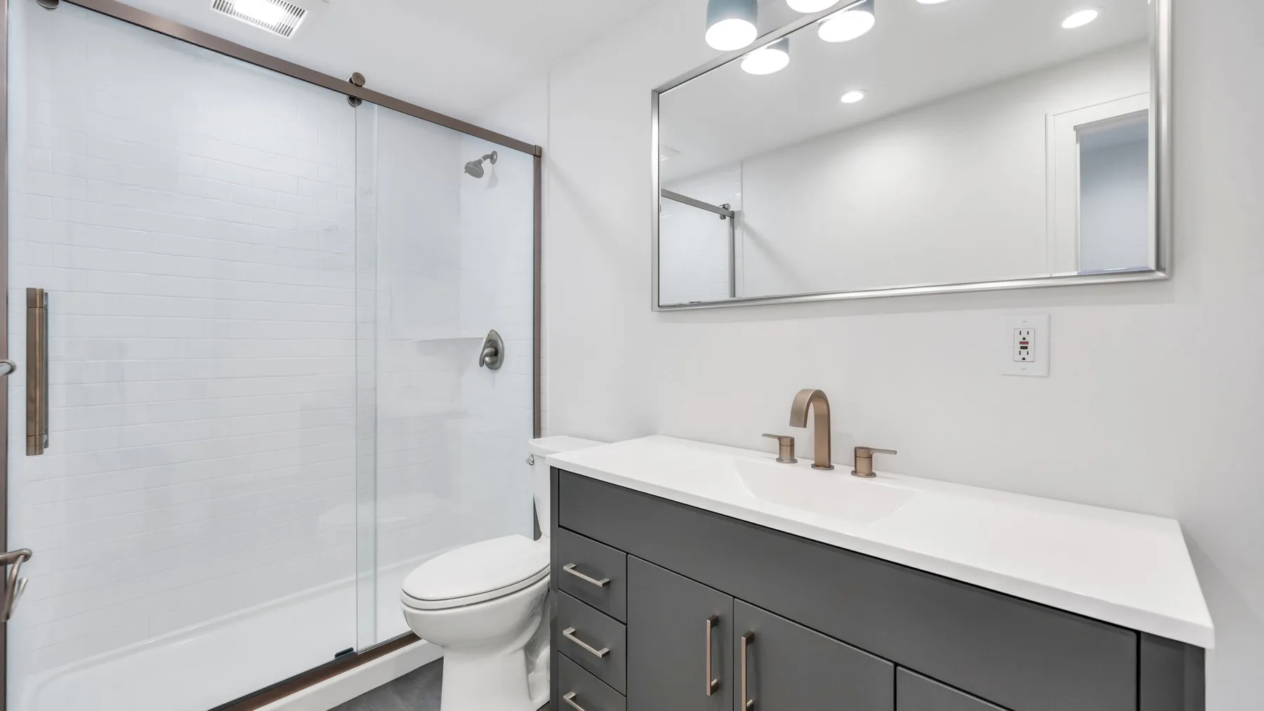 A bright bathroom with a glass shower, toilet, and vanity.