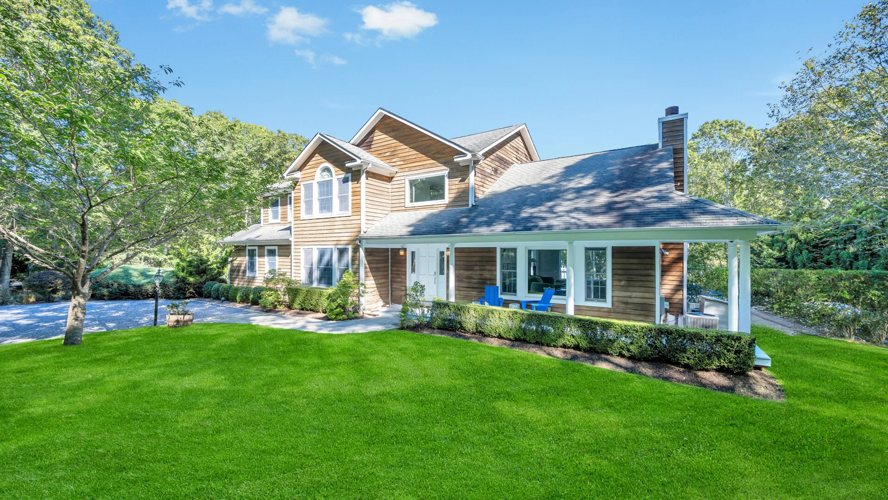 A two-story house with a covered patio sits beside a broad green lawn.