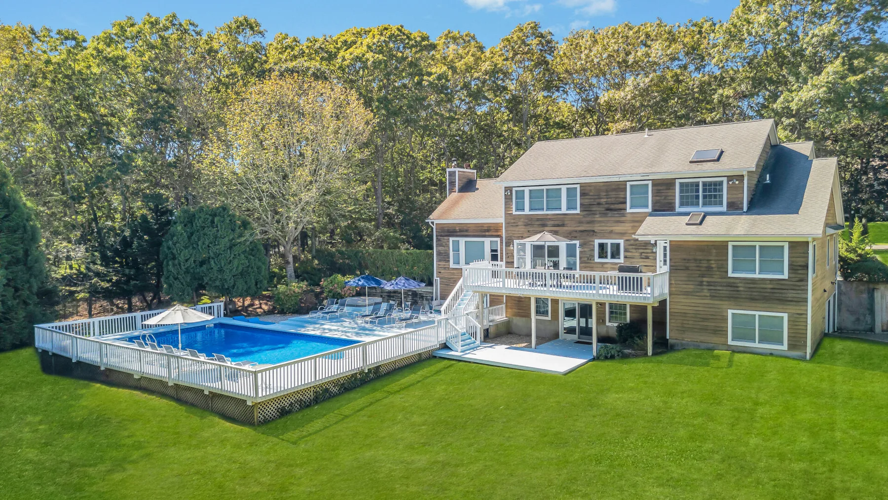 A large house overlooks a fenced outdoor swimming pool and a broad green lawn.