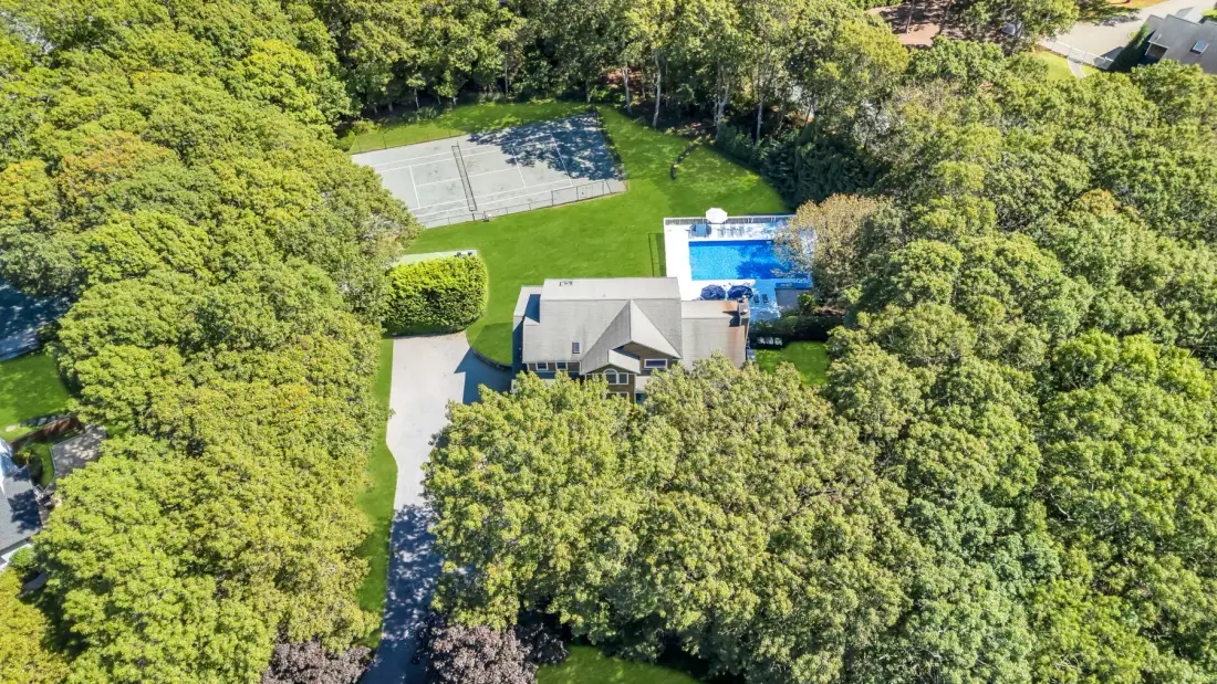 An aerial view shows a house, swimming pool, and tennis court among trees.