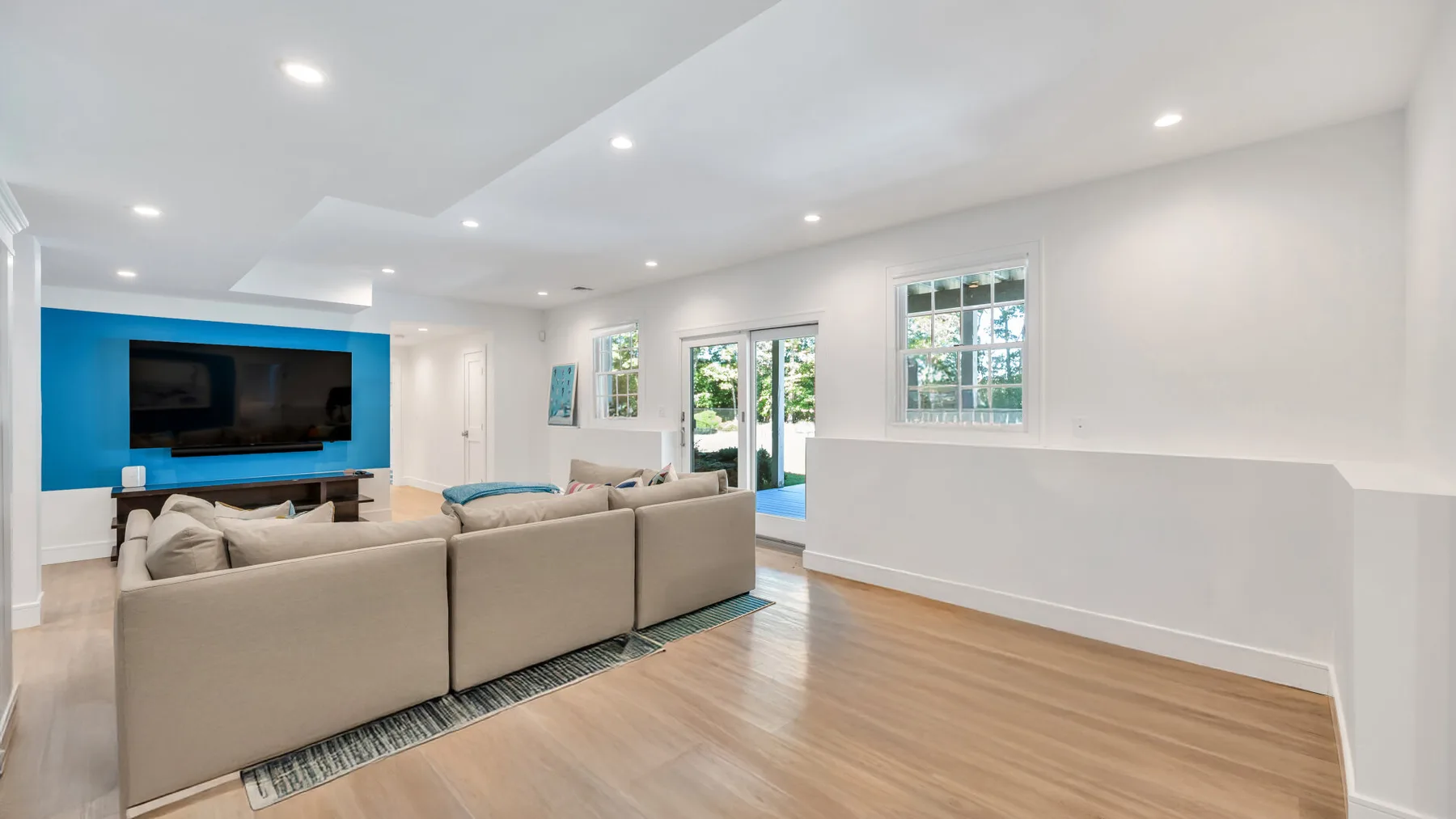A bright living room has seating facing a television on a blue accent wall.