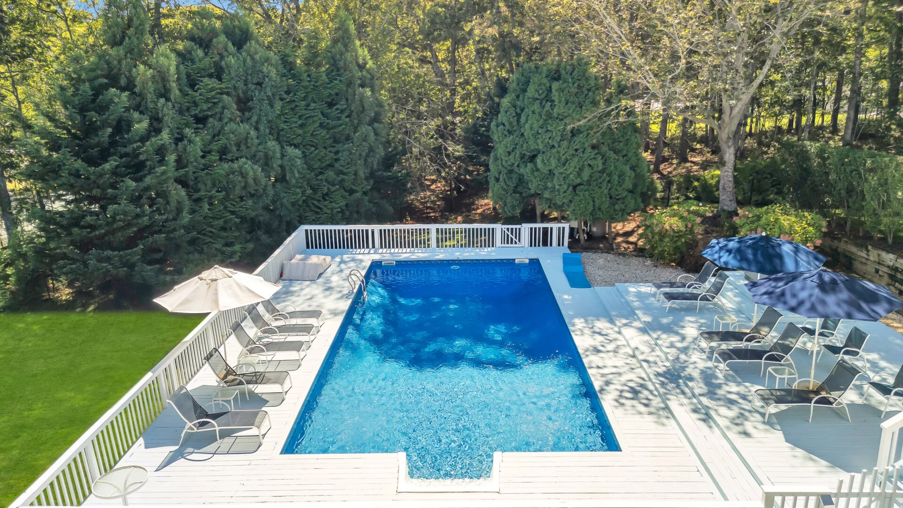 An outdoor swimming pool is surrounded by a deck with lounge seating and trees.