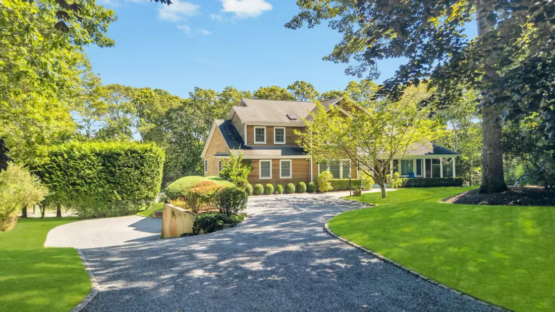 A large house stands beside a curved driveway, with trees and landscaped lawns.