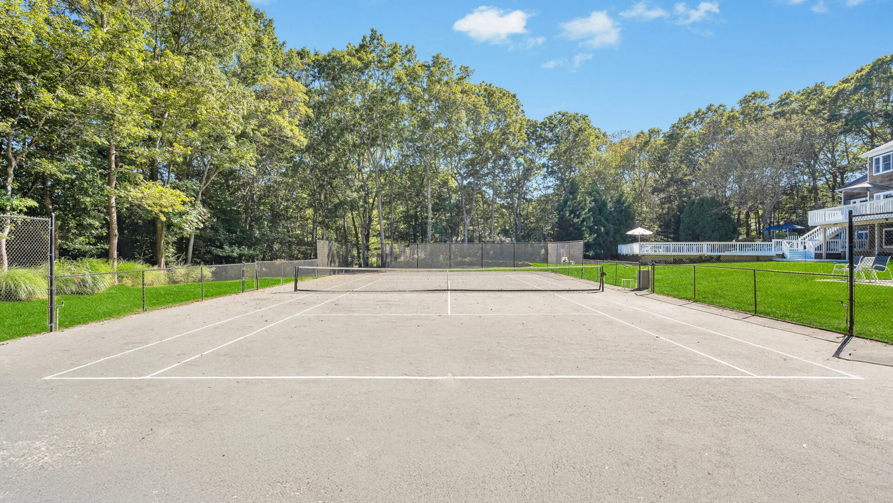 An outdoor tennis court is surrounded by green lawns and trees.