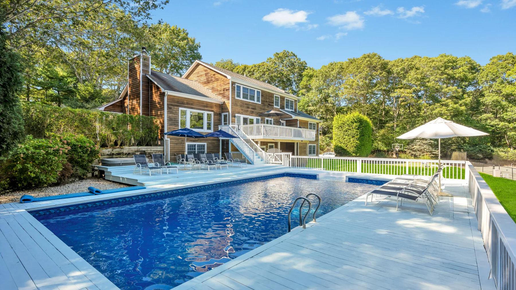 A swimming pool beside a wooden deck, with a house and trees behind it.