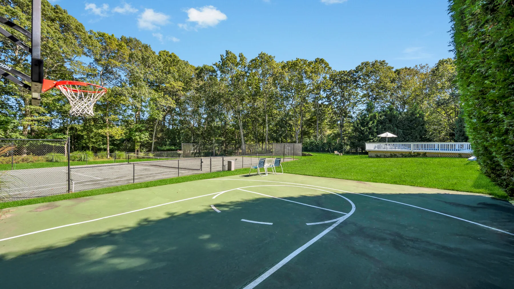 An outdoor basketball court beside a fenced tennis court and grassy field.