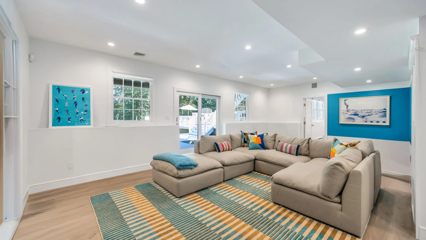 A bright living room with sectional seating and a colorful striped rug.
