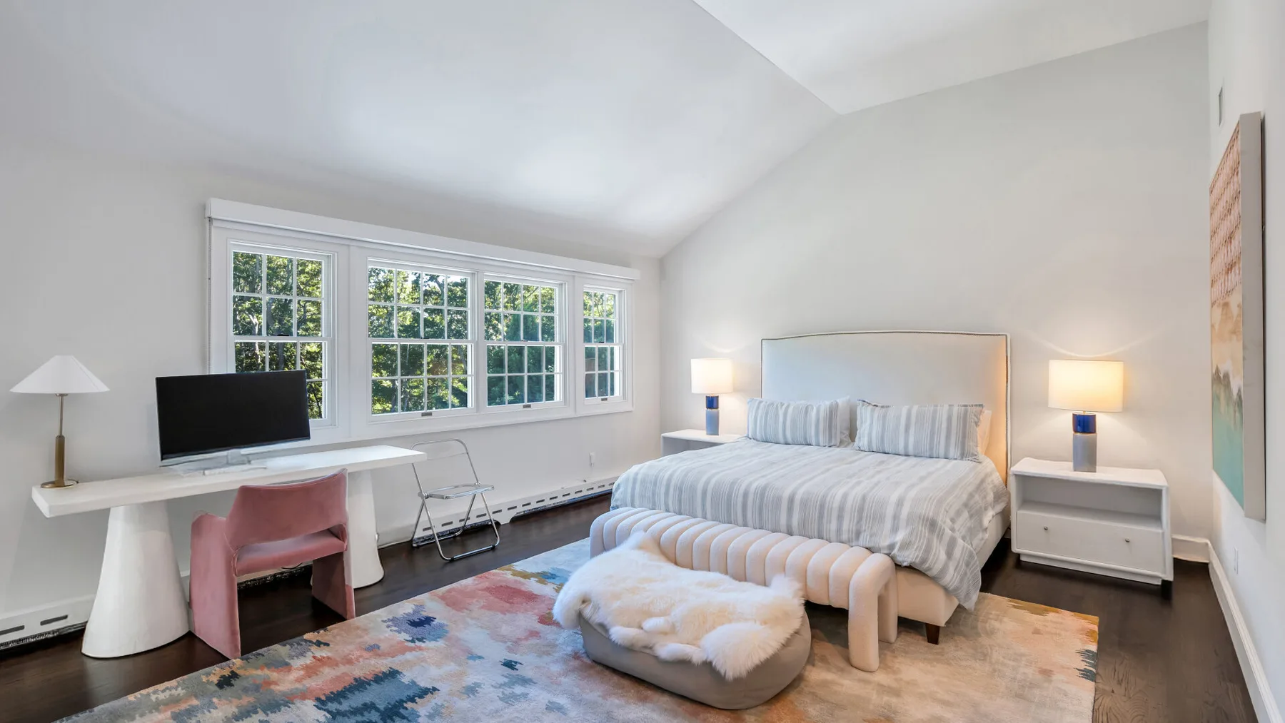 A bright bedroom with a bed, bedside tables, and large windows.