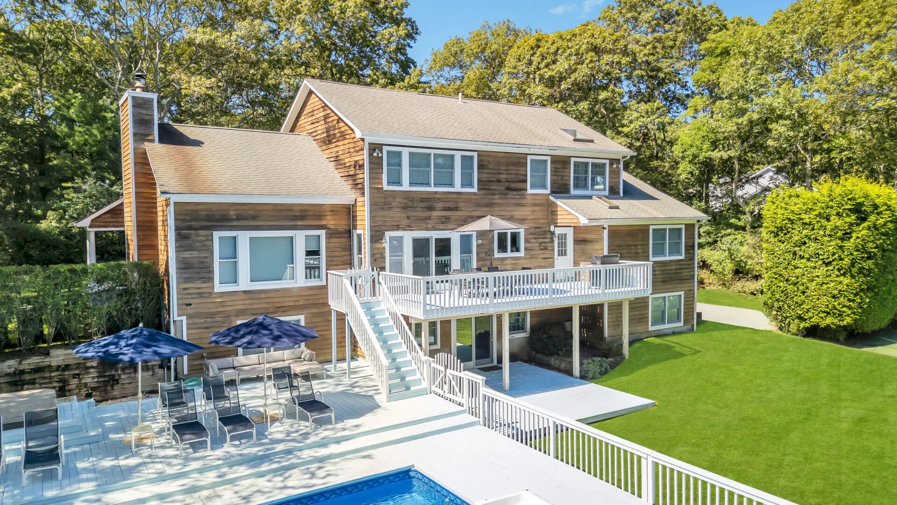 A large house overlooks a swimming pool, patio seating, and a broad lawn.