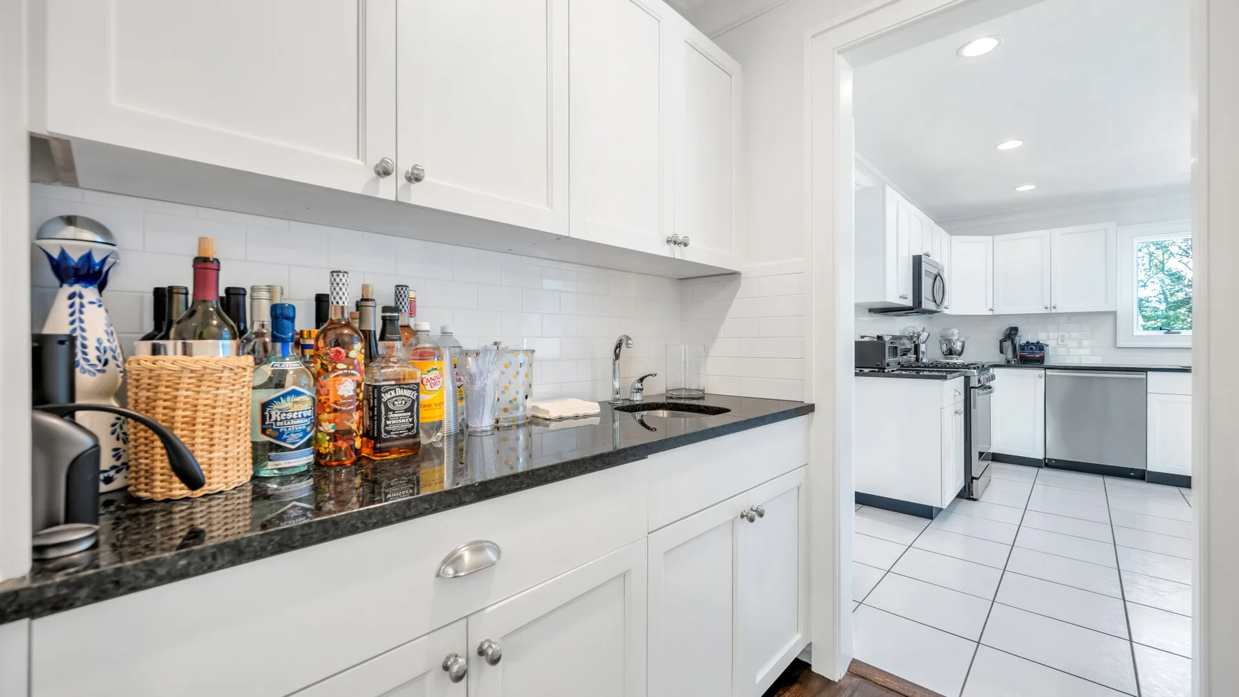 A bright kitchen with white cabinets, dark countertops, and a tiled floor.